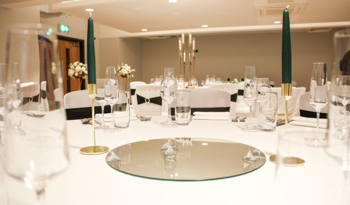 A round table set for an event, with a white tablecloth, elegant glassware, a mirror centrepiece.